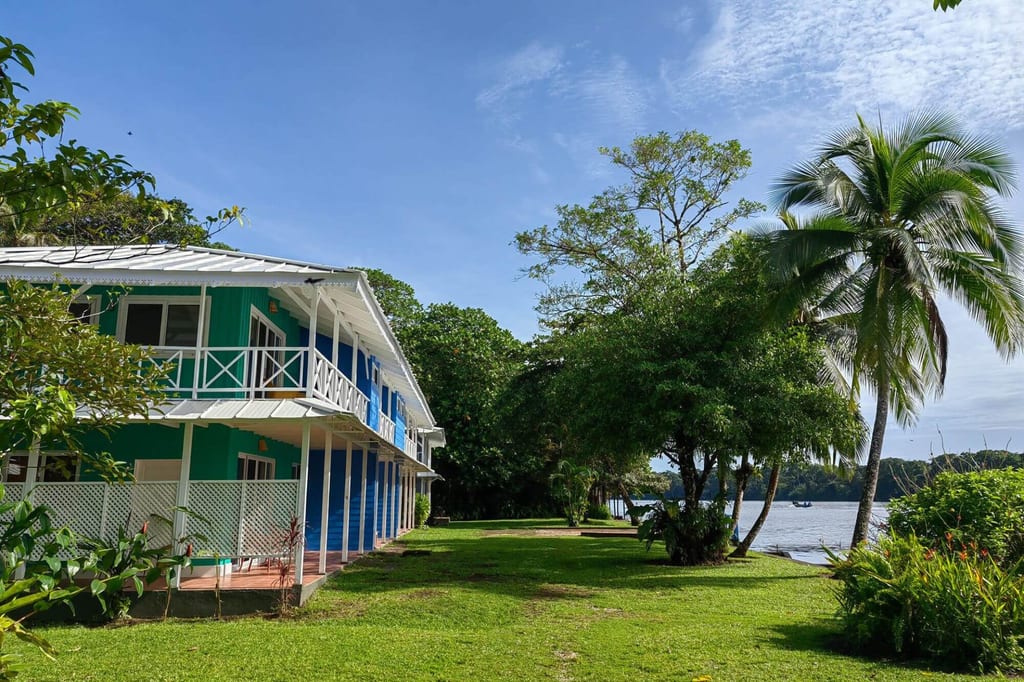 Buntes zweistöckiges Gästehaus mit Veranda an einem grünen Wasserufer bei blauem Himmel