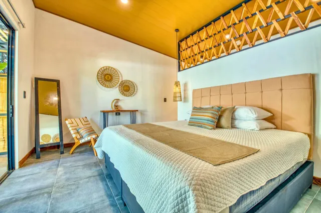 Helles Schlafzimmer mit großem Doppelbett, dekorativen Kissen, Spiegel und warmen Holzakzenten.