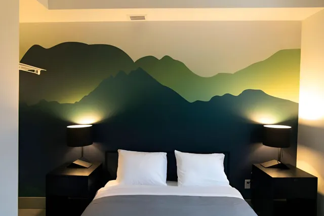 Schlafzimmer mit Doppelbett vor einer Wandmalerei aus stilisierten Bergen und zwei warm beleuchteten Nachttischlampen.
