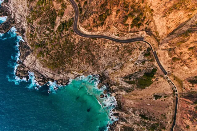 Drohnenaufnahme einer kurvigen Küstenstraße an felsiger Klippe mit türkisfarbenem Meer