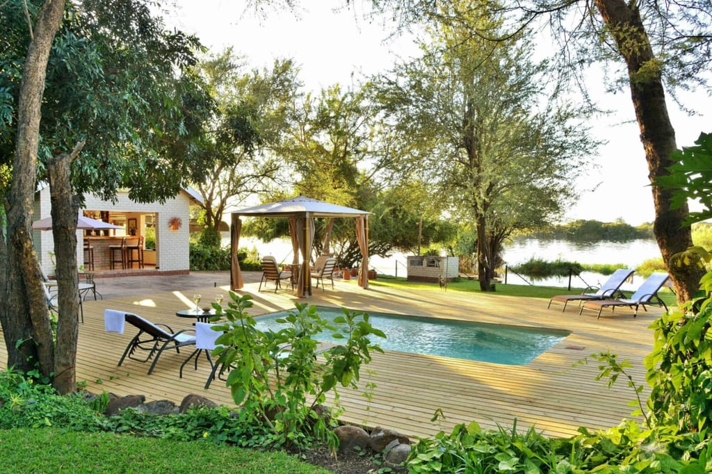 Pool auf Holzdeck mit Liegestühlen, Pavillon und Seeufer im warmen Spätnachmittagslicht.