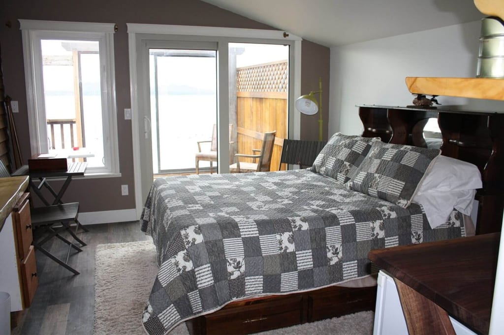 Gemütliches Schlafzimmer mit Doppelbett, grauer Steppdecke und Schiebetür zur Terrasse