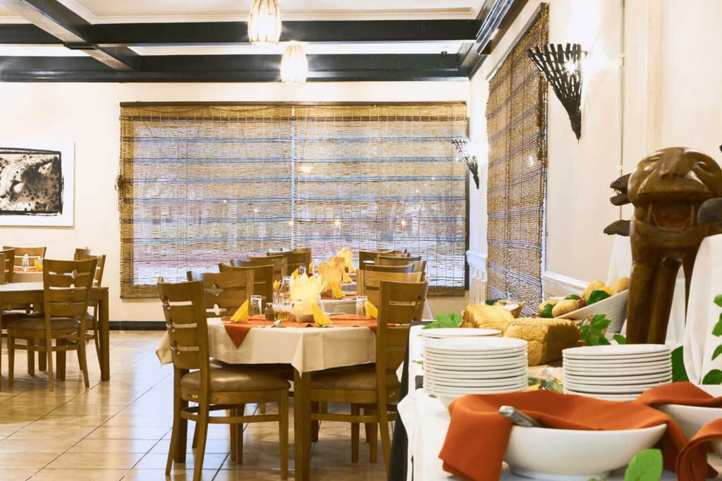 Restaurantinnenraum mit Buffet, gedeckten Tischen und Bambusjalousien, warme Beleuchtung.
