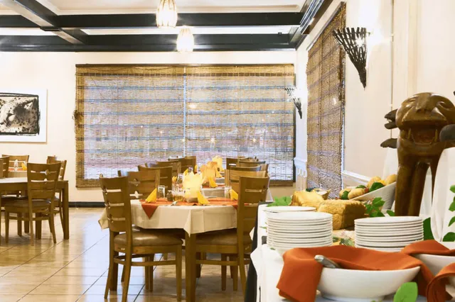 Restaurantinnenraum mit Buffet, gedeckten Tischen und Bambusjalousien, warme Beleuchtung.