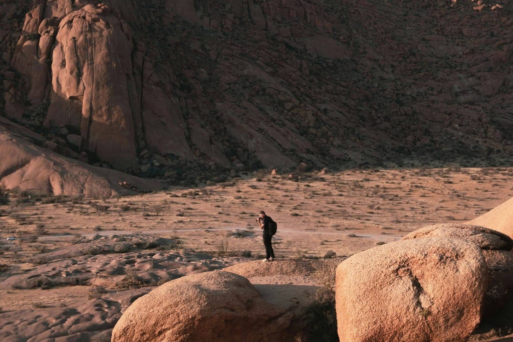 Einzelner Fotograf mit Rucksack in weiter Fels- und Wüstenlandschaft im warmen Seitenlicht.