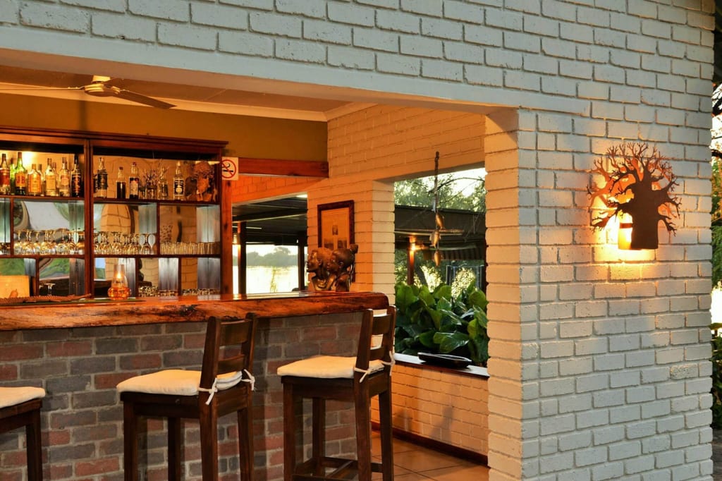 Innenraum einer gemütlichen Bar mit Holztheke, Barhockern und warmem Abendlicht