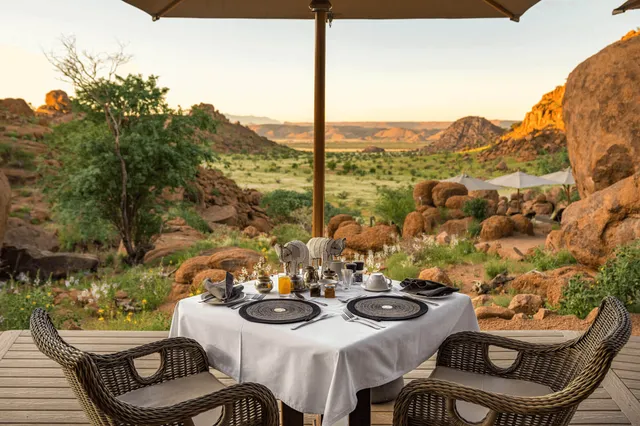 Gedeckter Frühstückstisch auf Terrasse mit Blick ins felsige Tal im goldenen Morgenlicht.