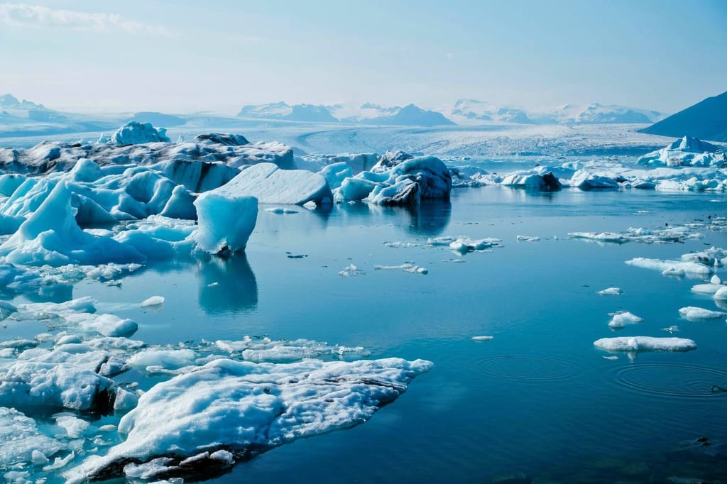 Gletscherlagune mit treibenden Eisbergen und spiegelndem Wasser unter klarem Tageshimmel