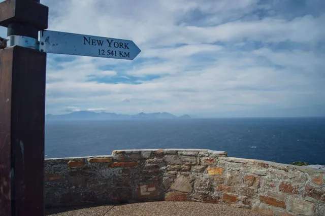 Blick über steinerne Brüstung aufs Meer, links Richtungsschild mit „New York 12 541 KM“