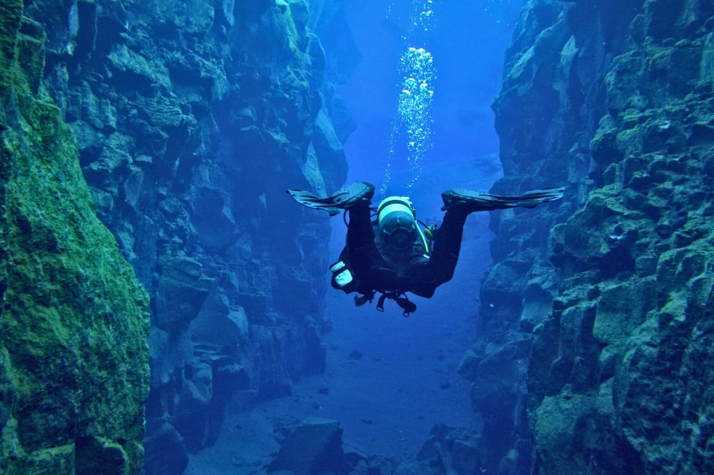 Ein Taucher schwimmt zwischen hohen Unterwasserfelsen in klarem blauem Wasser.