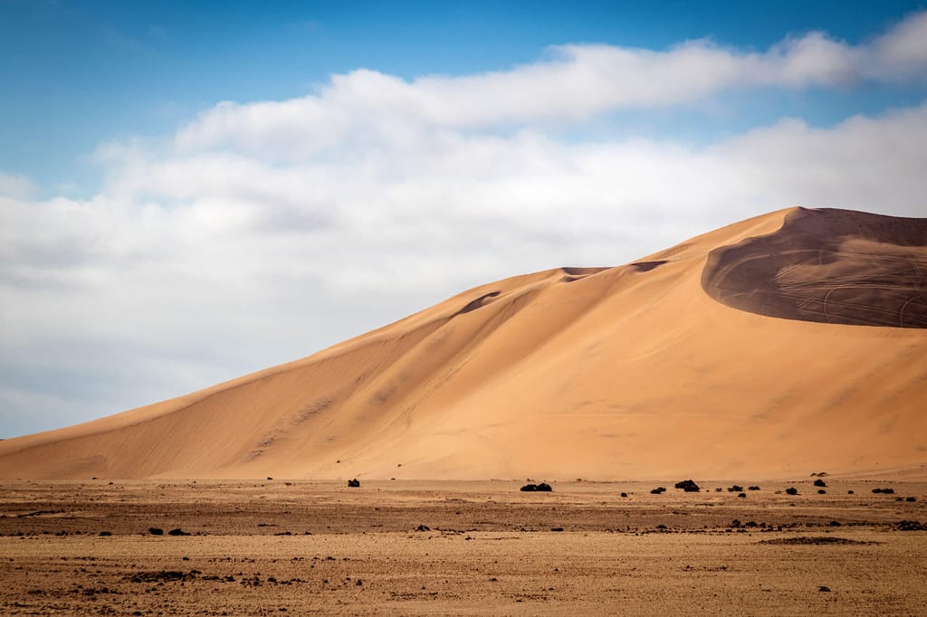 Große Sanddüne in einer weiten Wüstenlandschaft unter hellem, leicht bewölktem Himmel.