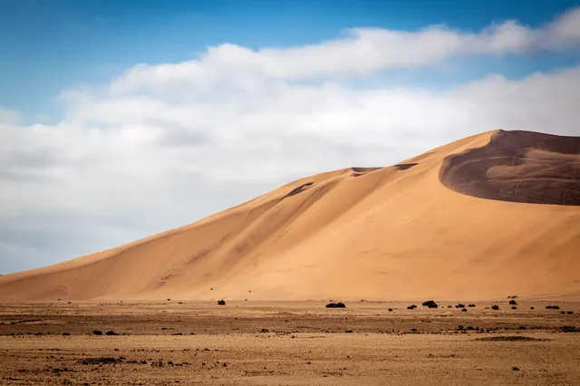 Große Sanddüne in einer weiten Wüstenlandschaft unter hellem, leicht bewölktem Himmel.