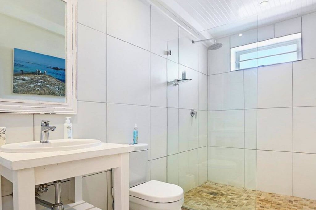 Helles modernes Badezimmer mit Glasdusche, Mosaikboden, Waschbecken und Toilette.