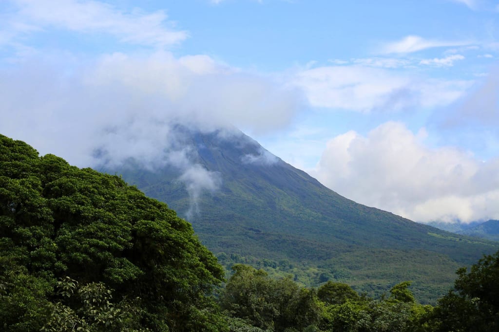 Blick auf einen teils wolkenverhangenen Berg über dichtem tropischem Regenwald am Tag.