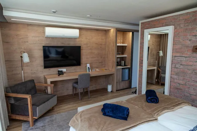 Modernes Hotelzimmer mit Bett, Schreibtisch, Fernseher und Backsteinakzent, warme Innenraumbeleuchtung.