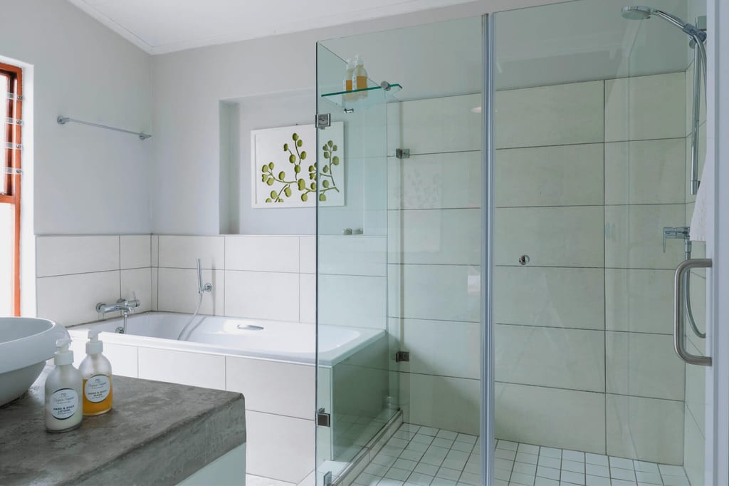 Helles modernes Badezimmer mit Badewanne, Glasdusche und Waschbecken, seitliche Perspektive.