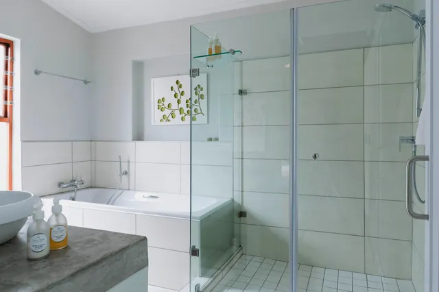 Helles modernes Badezimmer mit Badewanne, Glasdusche und Waschbecken, seitliche Perspektive.