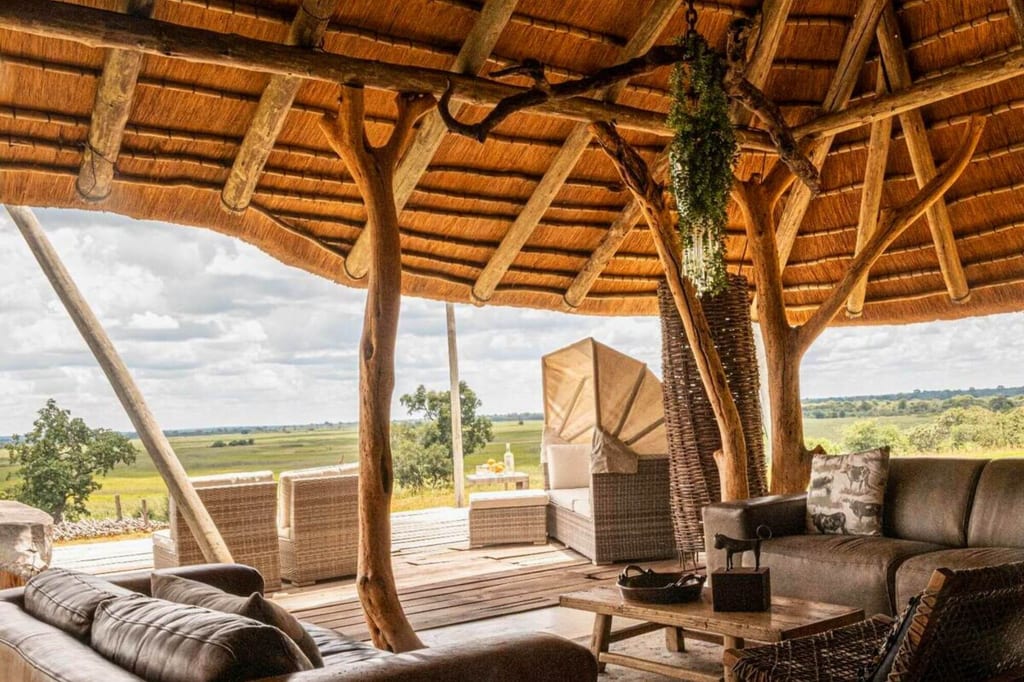 Offene Lodge-Lounge mit Strohdach und Blick auf weite Graslandschaft bei Tageslicht.