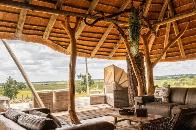 Offene Lodge-Lounge mit Strohdach und Blick auf weite Graslandschaft bei Tageslicht.
