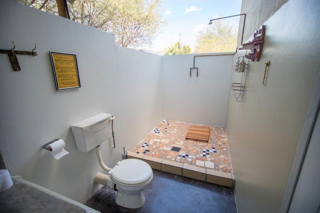 Freiluft-Badebereich mit Toilette, ebenerdiger Dusche und Mosaikfliesen unter offenem Himmel