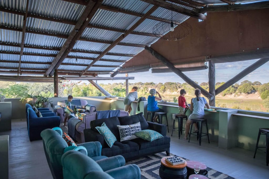 Offene Lounge mit Sofas, Personen am Geländer blicken auf Landschaft und Wasser im warmen Nachmittagslicht.