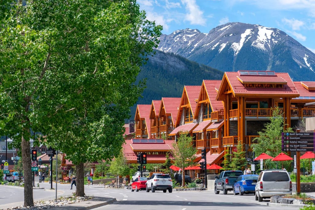Straßenszene mit holzchalets, Sonnenschirmen und schneebedeckten Bergen im Hintergrund