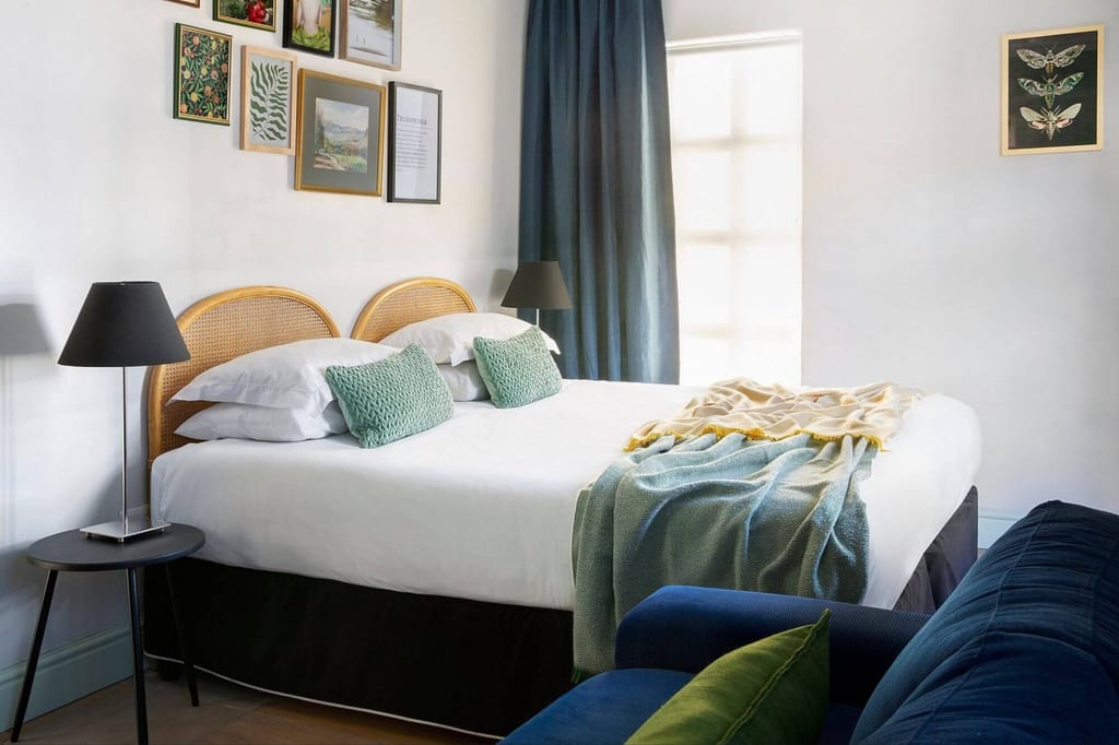 Helles Schlafzimmer mit Doppelbett, grünen Kissen, Wandbildern und weichem Tageslicht.