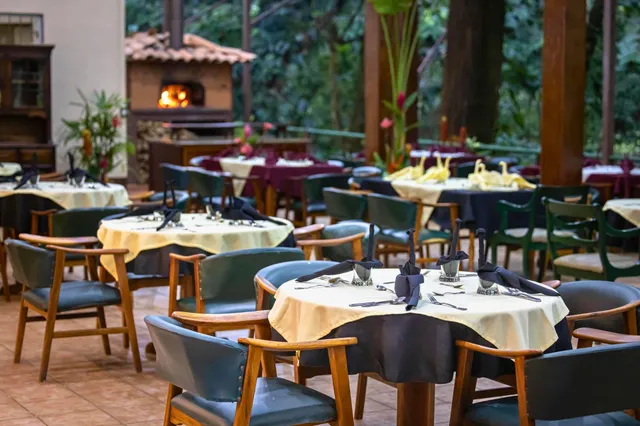 Gedeckte Restaurantterrasse mit runden Tischen, Holzstühlen und brennendem Holzofen im Hintergrund