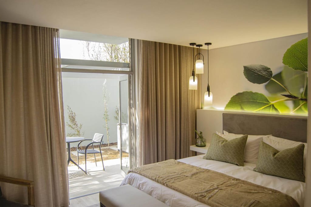Helles Hotelzimmer mit Doppelbett, geöffneten Terrassentür und kleinem Tisch auf der Terrasse.