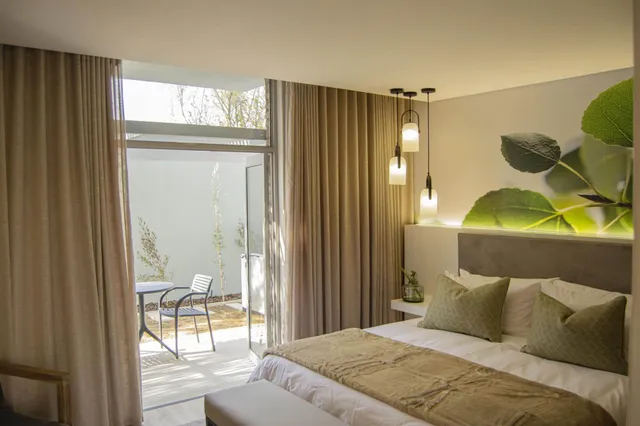 Helles Hotelzimmer mit Doppelbett, geöffneten Terrassentür und kleinem Tisch auf der Terrasse.