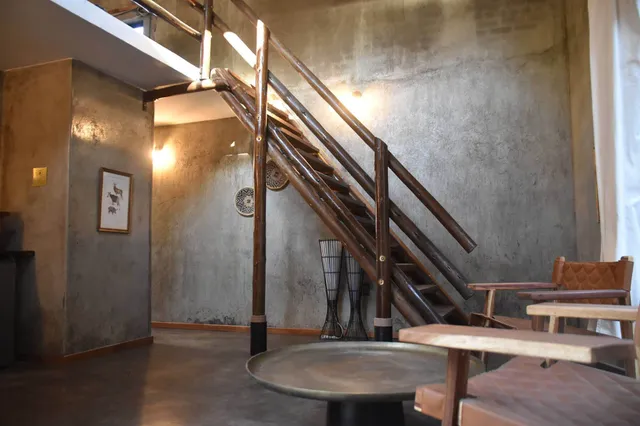 Gemütlicher Innenraum mit rustikaler Holztreppe, Betonwänden und Sitzmöbeln, warm beleuchtet.