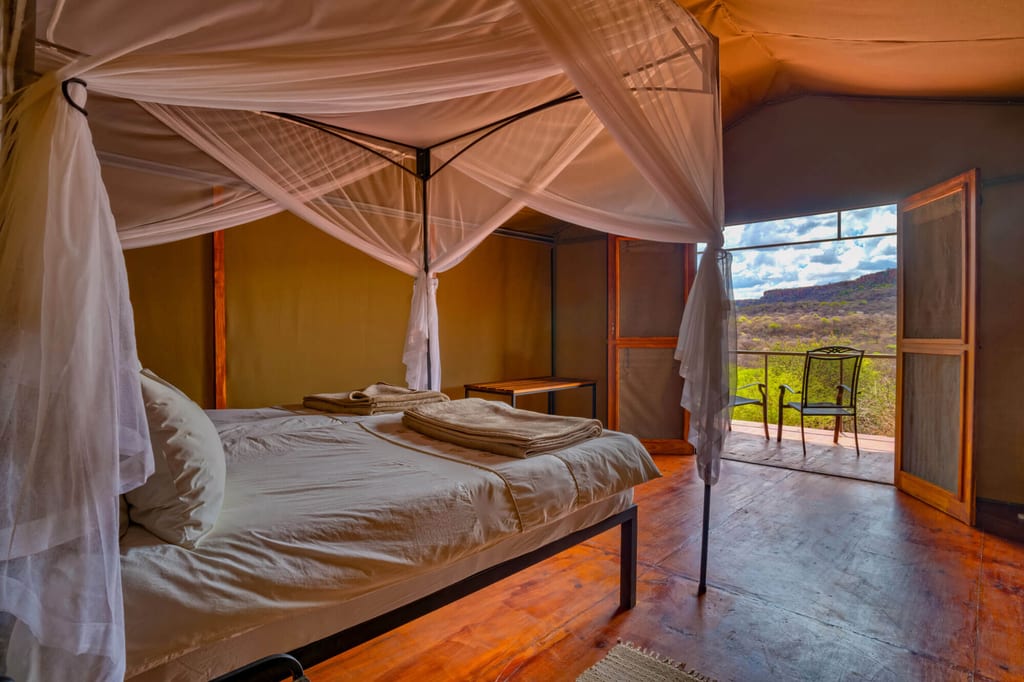 Safarizelt-Innenraum mit Himmelbett, Moskitonetz und Blick auf hügelige Landschaft von der Veranda