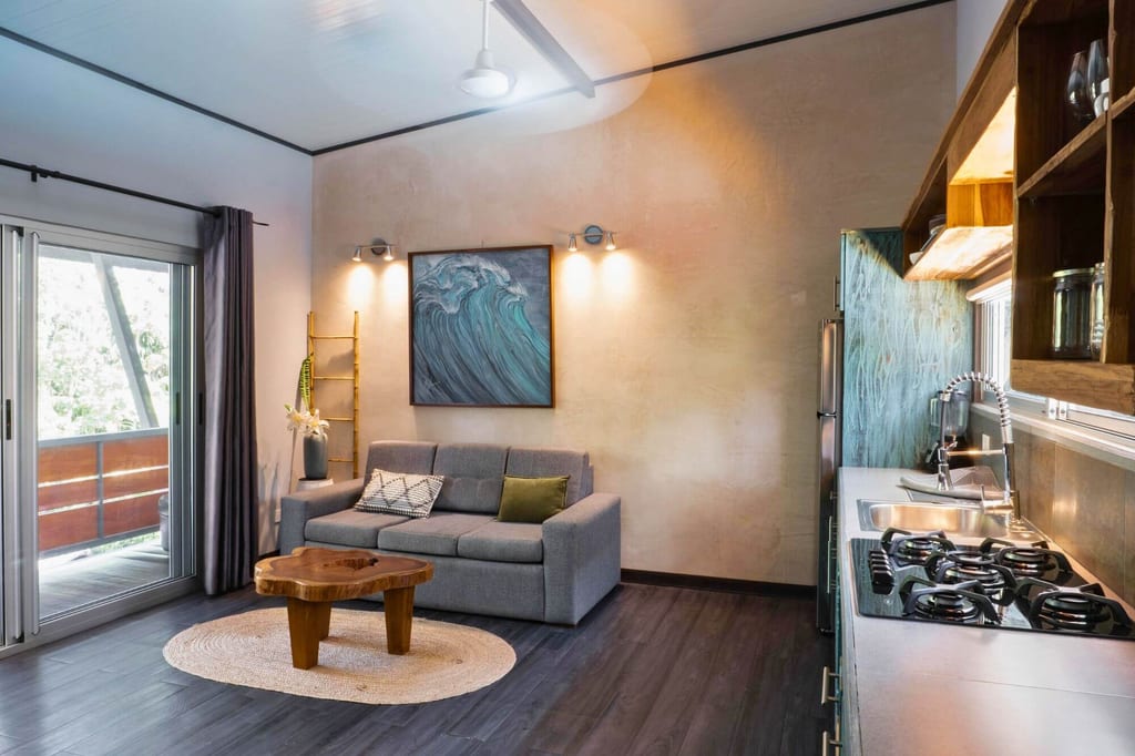 Offenes Wohnzimmer mit grauem Sofa, Holztisch und angrenzender Küche, Tageslicht vom Balkon