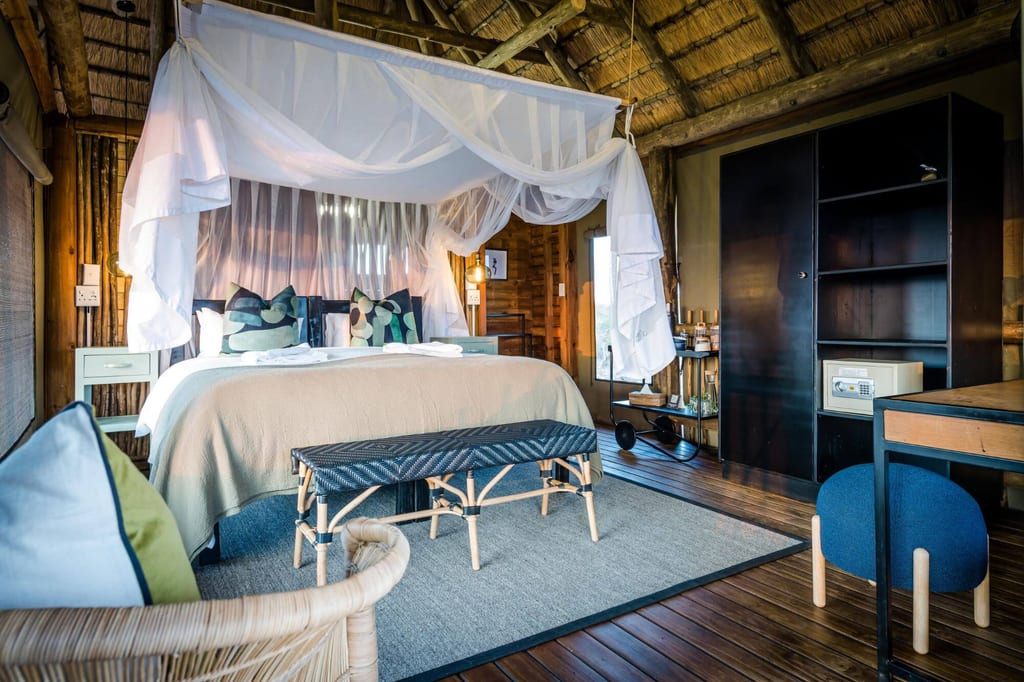Gemütliches Lodge-Schlafzimmer mit Bett, Moskitonetz und Strohdach, warm beleuchtet