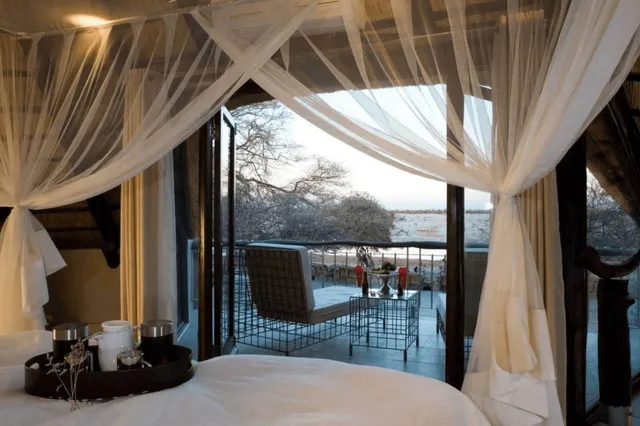 Innenansicht eines Lodgebetts mit Moskitonetz und offenem Blick auf Terrasse und weite Baumlandschaft.