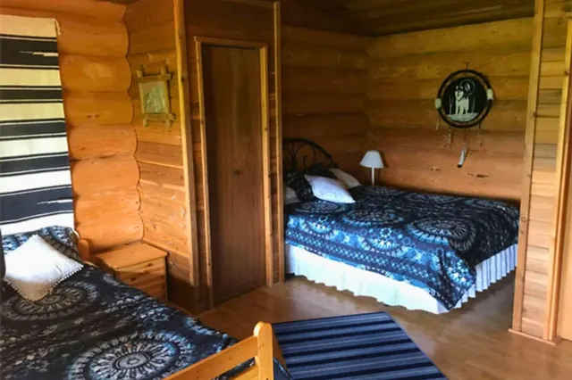 Rustikales Schlafzimmer mit zwei Betten, blauen Decken und Holzwänden, warmes Tageslicht