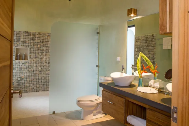 Modernes Badezimmer mit Waschbecken, Toilette, Milchglasscheibe und Mosaikfliesen, Dekoration mit orangefarbenen Blüten.