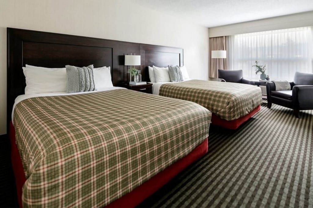 Helles Hotelzimmer mit zwei Doppelbetten, Sitzecke und großem Fenster.