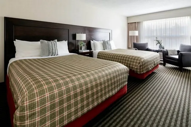 Helles Hotelzimmer mit zwei Doppelbetten, Sitzecke und großem Fenster.