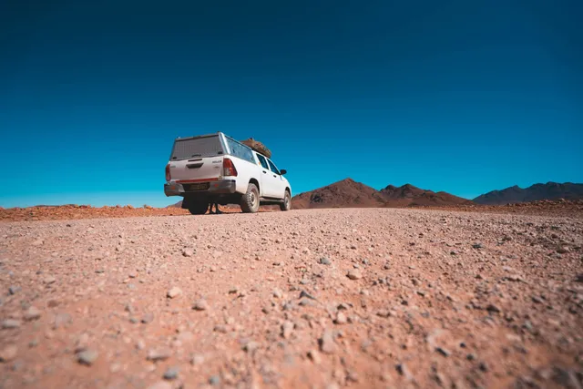 Weißer Pickup auf Schotterpiste in karger Berglandschaft unter klarem blauen Himmel