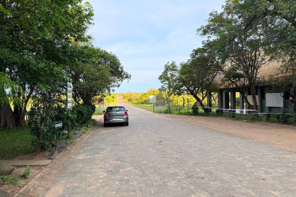 Gepflasterte Zufahrtsstraße mit geparktem Auto, Bäumen und Eingangsgebäude bei klarem Tageslicht.