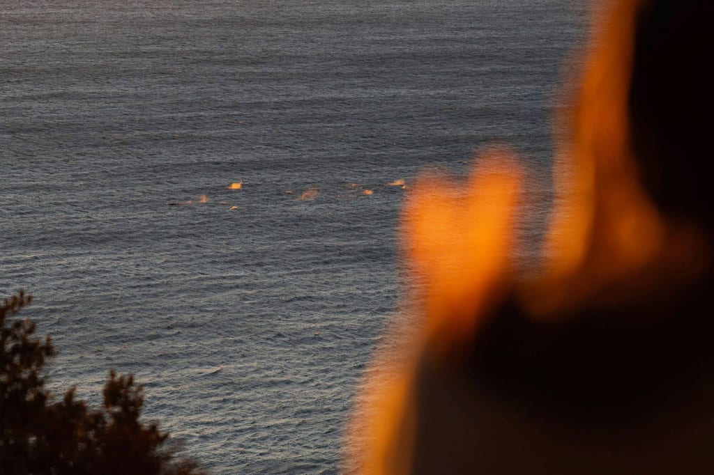 Blick aufs Meer im warmen Abendlicht, unscharfe Personen-Silhouette im Vordergrund und Gischt am Horizont.