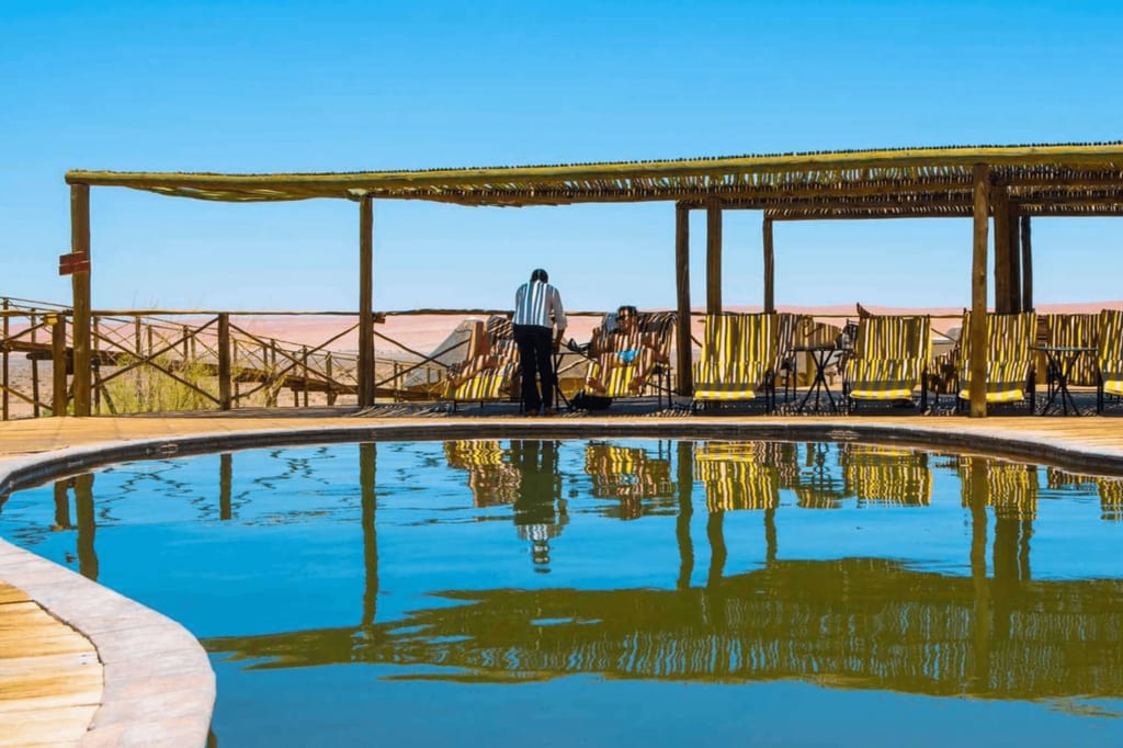 Freiluft-Pool mit Liegestühlen und zwei Personen, klare Spiegelung der Pergola im Wasser.