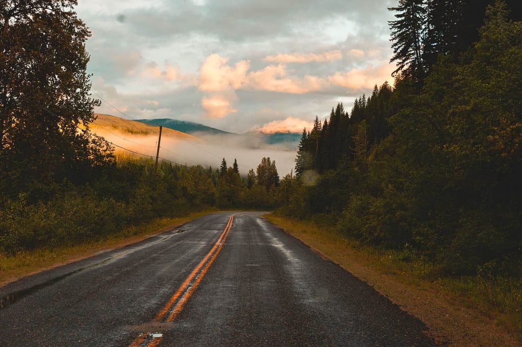 Nasse Landstraße führt ins neblige Tal zwischen Wäldern und Bergen im Wells Gray Provincial Park, Kanada.