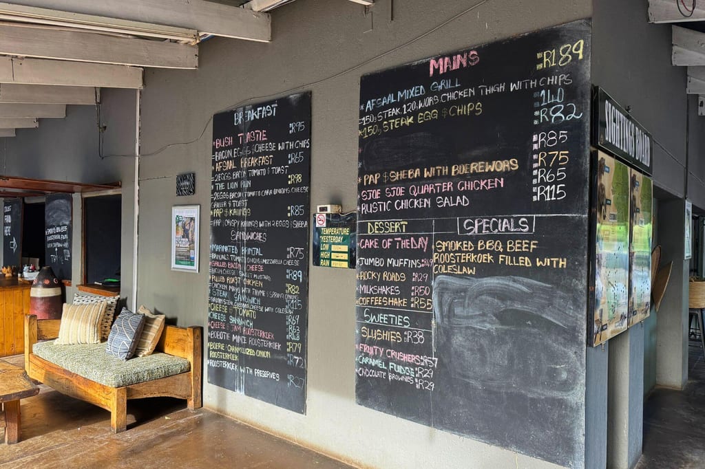 Café-Innenraum mit großen Kreidetafeln als Menü und einer rustikalen Holzbank mit Kissen, Tageslicht fällt ein.