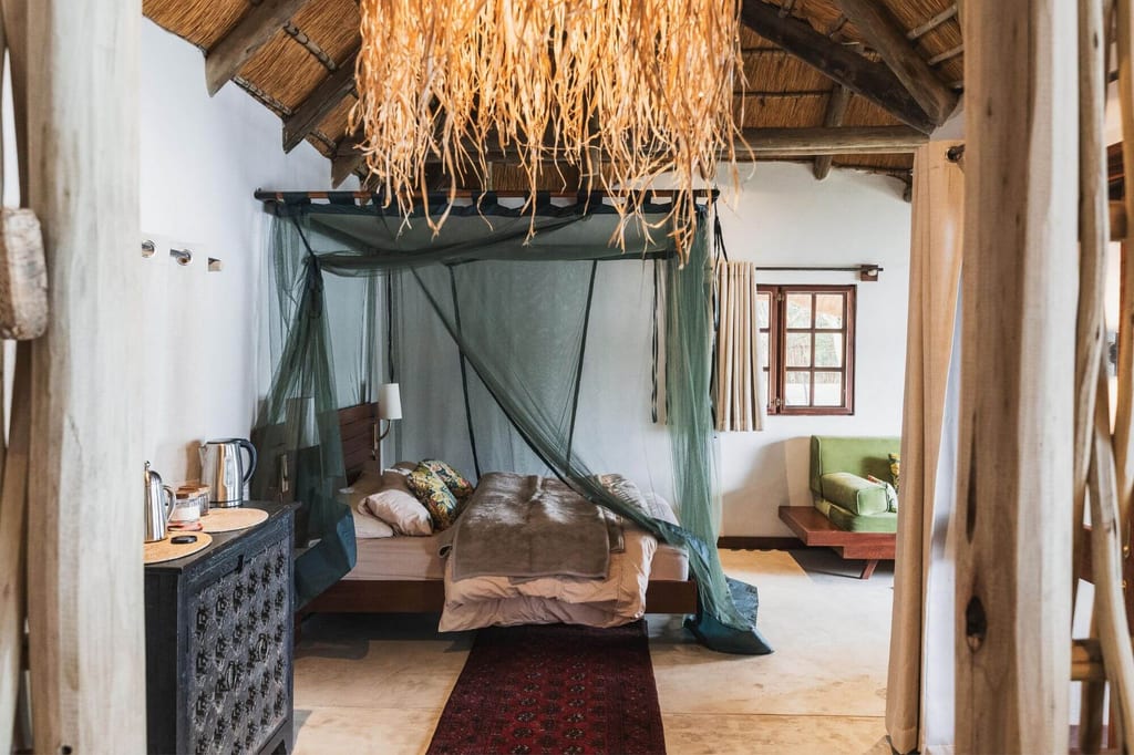 Rustikales Schlafzimmer mit grünem Moskitonetz und Strohdach, Blick vom Türrahmen