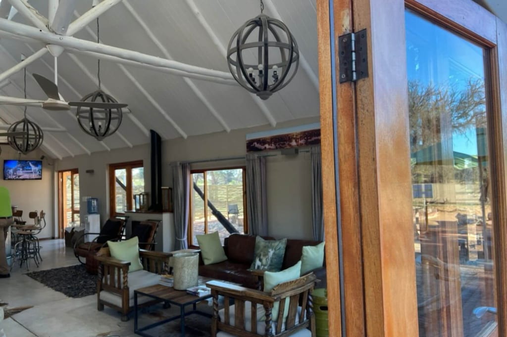 Helle Lodge-Lounge mit Holzmöbeln, hoher Decke und offenem Glas-Tür zur Terrasse