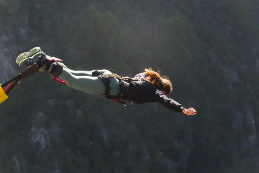 Person beim Bungee-Jumping waagerecht im Sprung vor bewaldeter Felswand