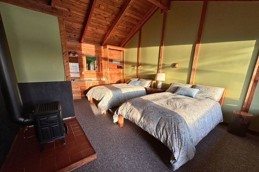 Rustikales Schlafzimmer mit zwei Doppelbetten, Kaminofen und warmem seitlichen Sonnenlicht