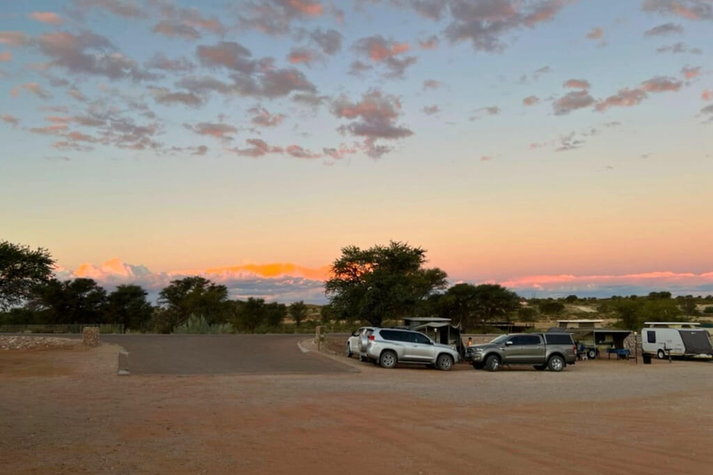 Campingplatz mit Geländewagen und Wohnanhängern bei pastellfarbenem Sonnenuntergang